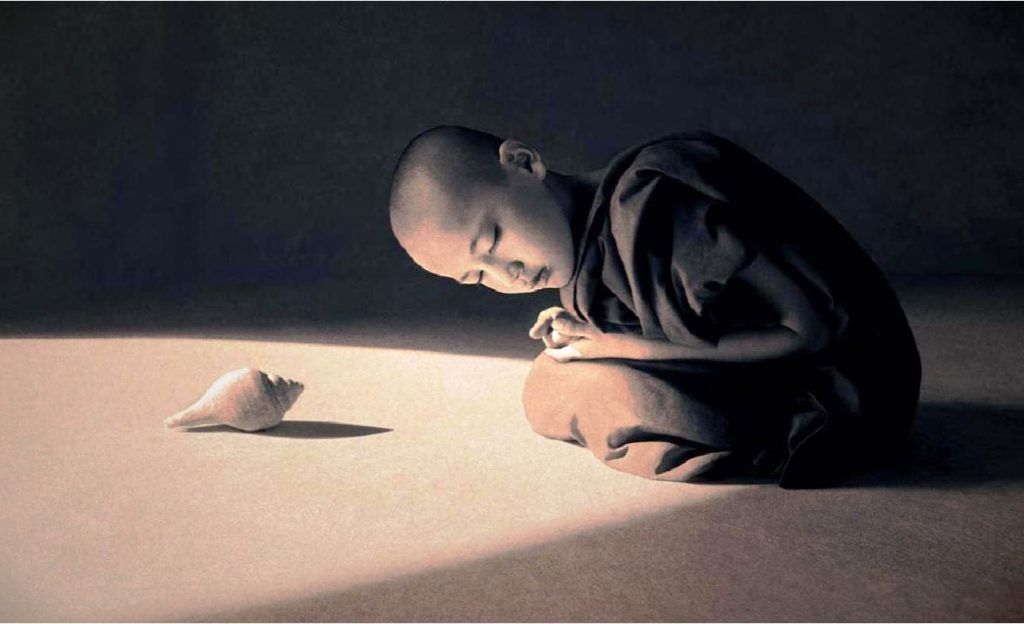 Na imagem, um pequeno monge budista está sentado e escutando, com atenção, som de uma concha. O momento presente é importante.